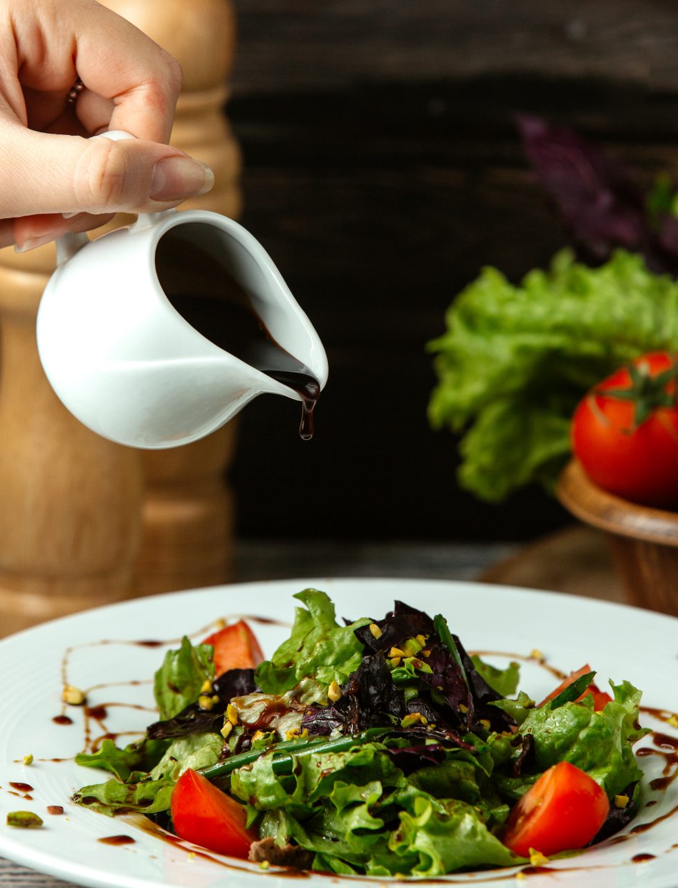 Dressing being poured onto a green salad with tomatoes.
