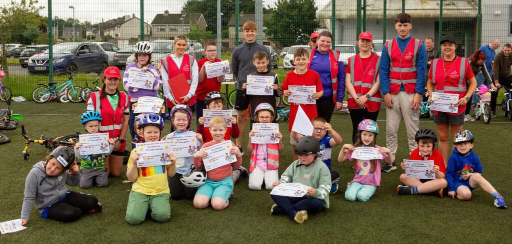 Group of young children hold their Learn 2 Cycle certificates on an astroturf pitch.